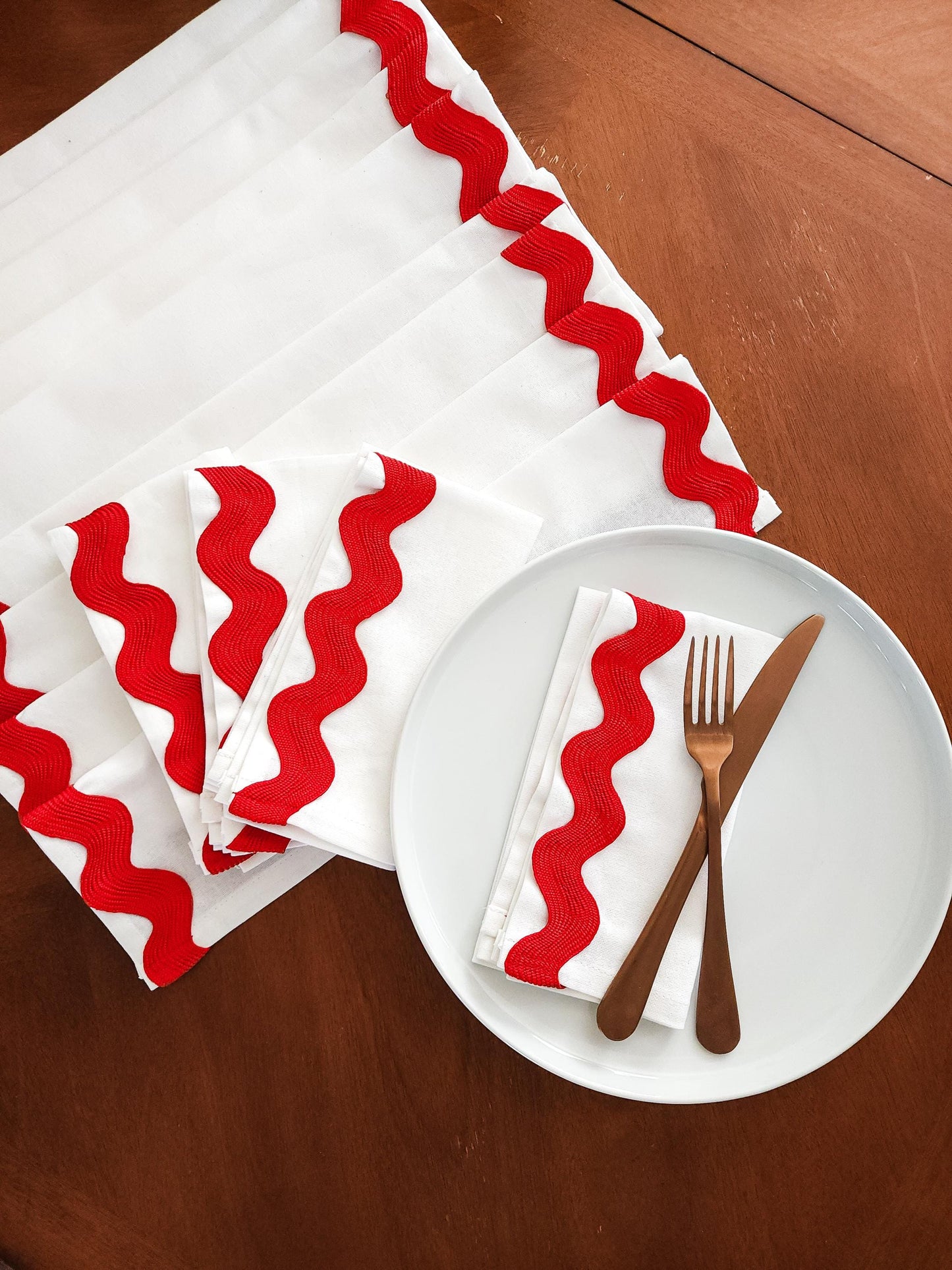 Red and white zigzag-patterned napkins and table runner on a wooden table with a plate, fork, and knife.