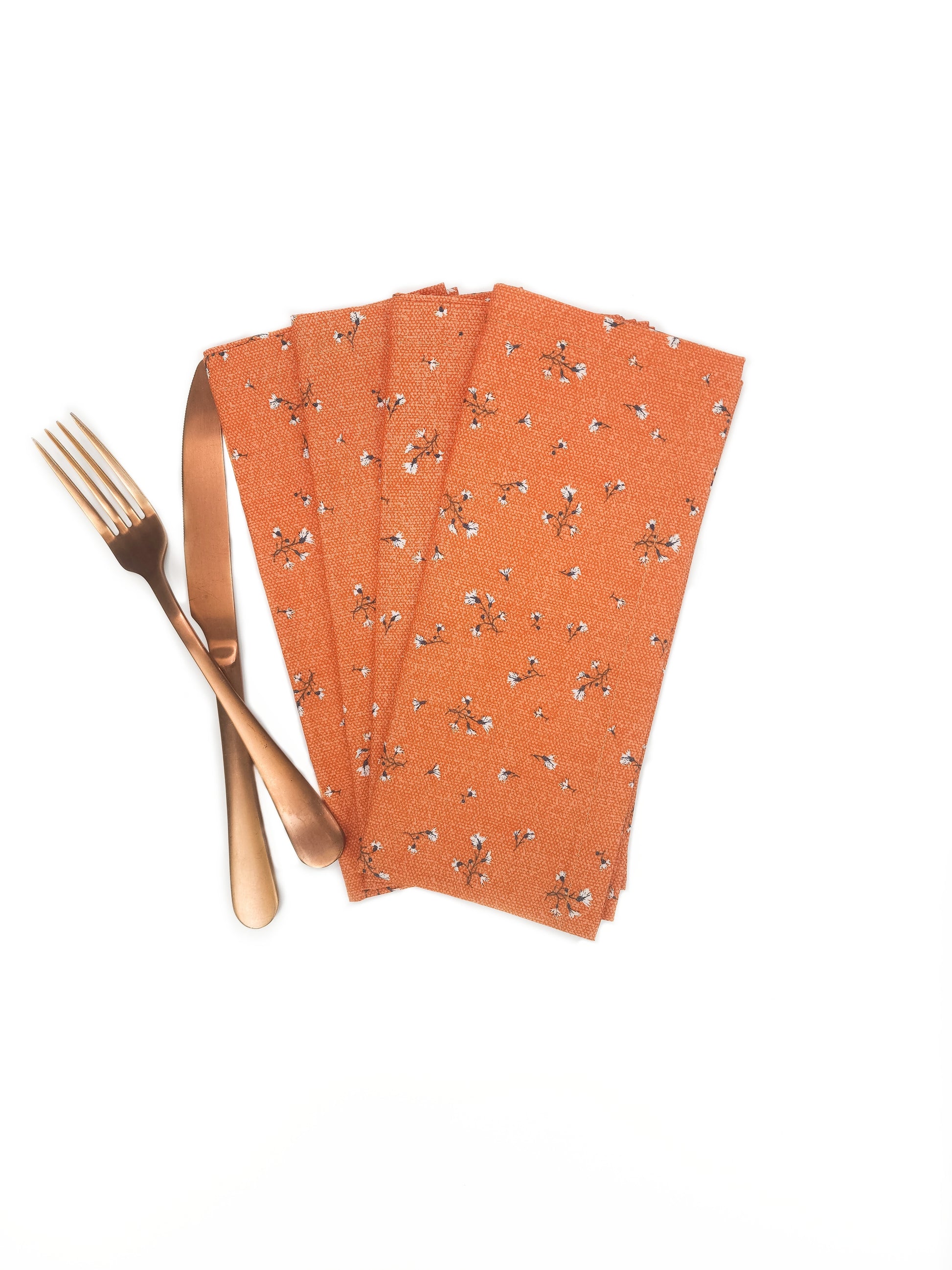 Set of orange napkins with floral pattern and gold fork on a white background